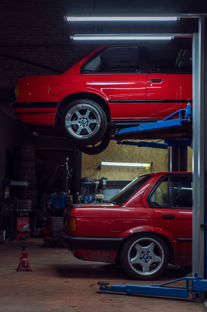 Two red cars in an auto shop, one raised on a lift